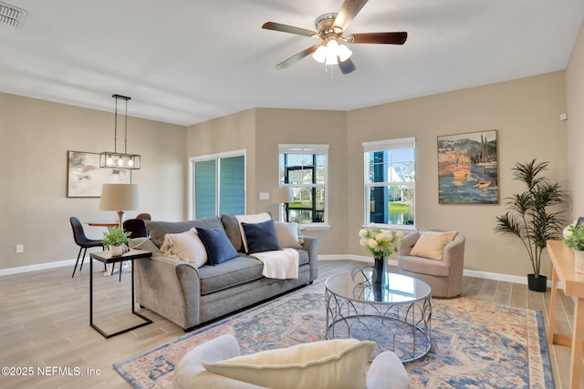 living room featuring wood finish floors, visible vents, baseboards, and ceiling fan