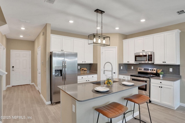 kitchen with visible vents, a sink, white cabinetry, stainless steel appliances, and wood tiled floor