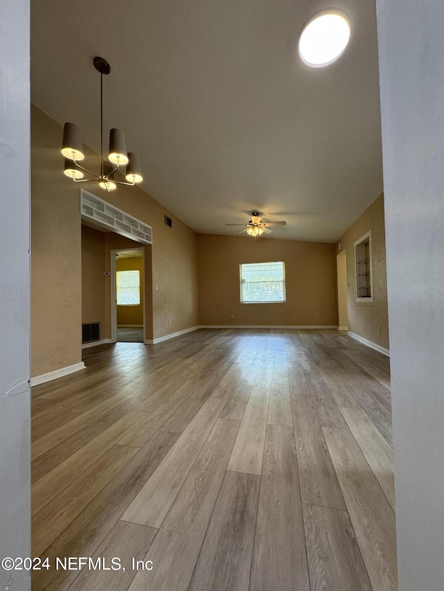 unfurnished living room featuring ceiling fan with notable chandelier and light hardwood / wood-style floors