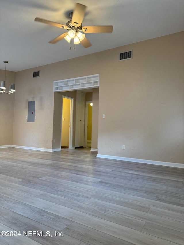 spare room with light wood-type flooring, ceiling fan with notable chandelier, and electric panel