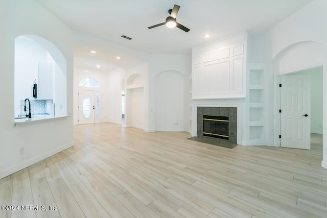 unfurnished living room with a fireplace, sink, light hardwood / wood-style floors, ceiling fan, and built in shelves