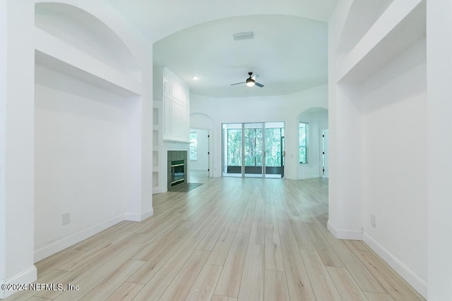 unfurnished living room featuring a tile fireplace, ceiling fan, and light wood-type flooring