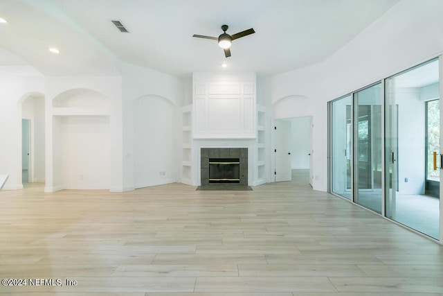 unfurnished living room featuring a tiled fireplace, built in features, ceiling fan, and light hardwood / wood-style flooring