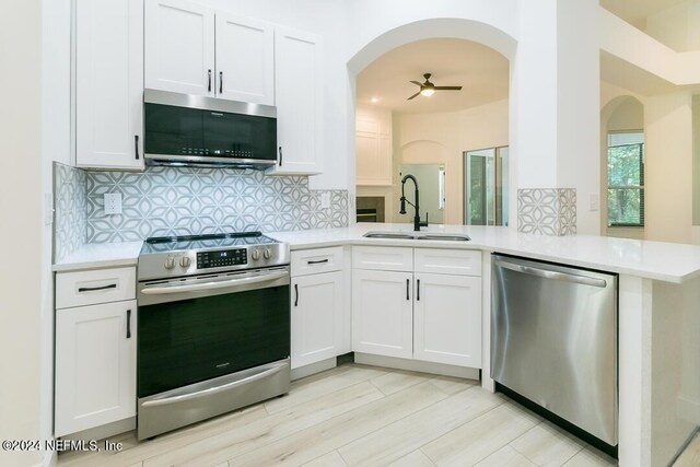 kitchen with tasteful backsplash, stainless steel appliances, sink, kitchen peninsula, and white cabinetry