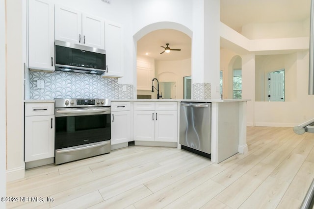 kitchen featuring white cabinetry, backsplash, stainless steel appliances, kitchen peninsula, and light wood-type flooring