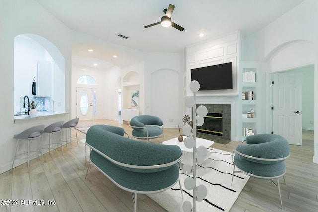 living room with built in shelves, ceiling fan, a fireplace, and light wood-type flooring