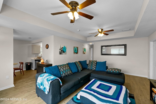 living room featuring ceiling fan, light wood-type flooring, and a raised ceiling