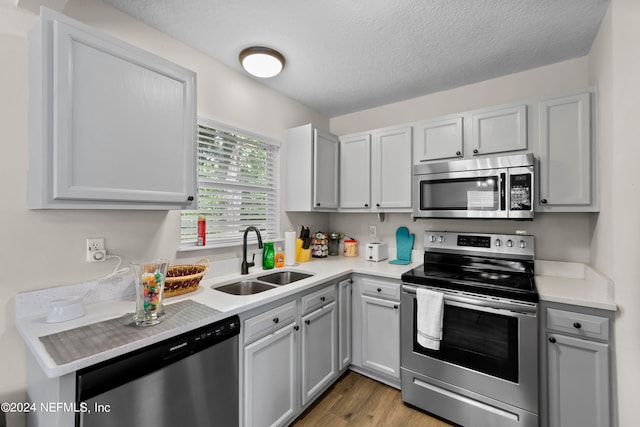 kitchen with stainless steel appliances, wood finished floors, a sink, and light countertops