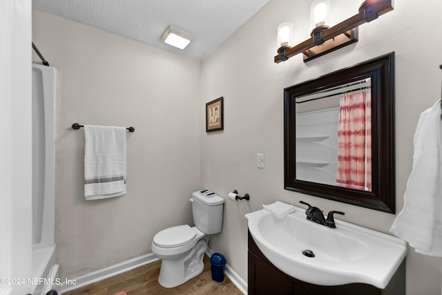 bathroom featuring toilet, a textured ceiling, vanity, wood finished floors, and baseboards