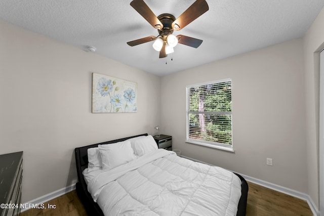 bedroom featuring ceiling fan, a textured ceiling, baseboards, and wood finished floors