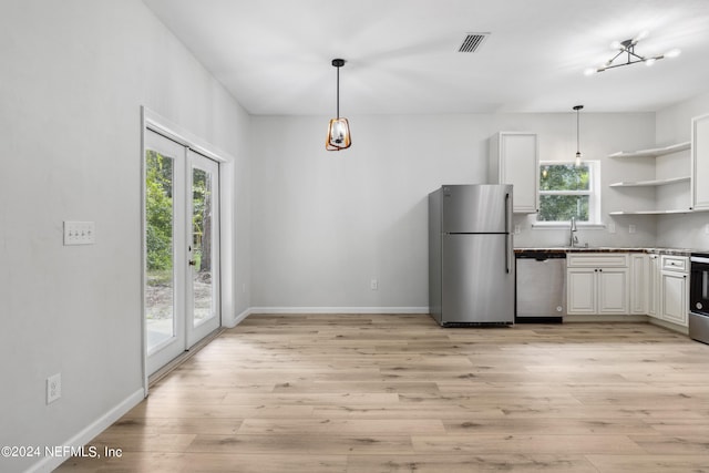 kitchen with white cabinetry, stainless steel appliances, hanging light fixtures, and light wood-type flooring