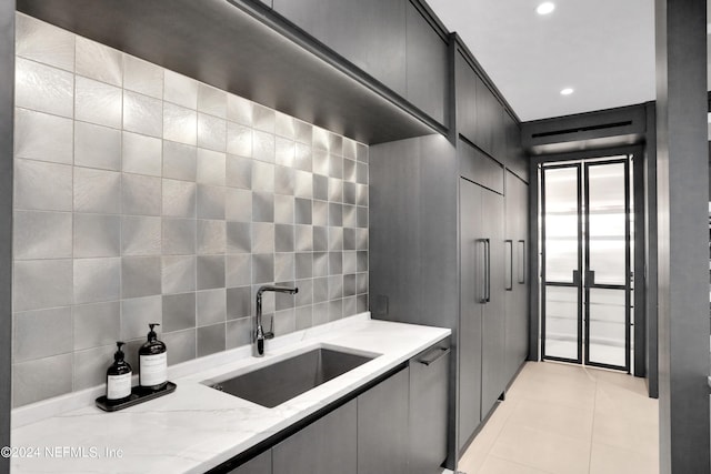 kitchen featuring sink, light stone counters, tasteful backsplash, tile walls, and light tile patterned floors