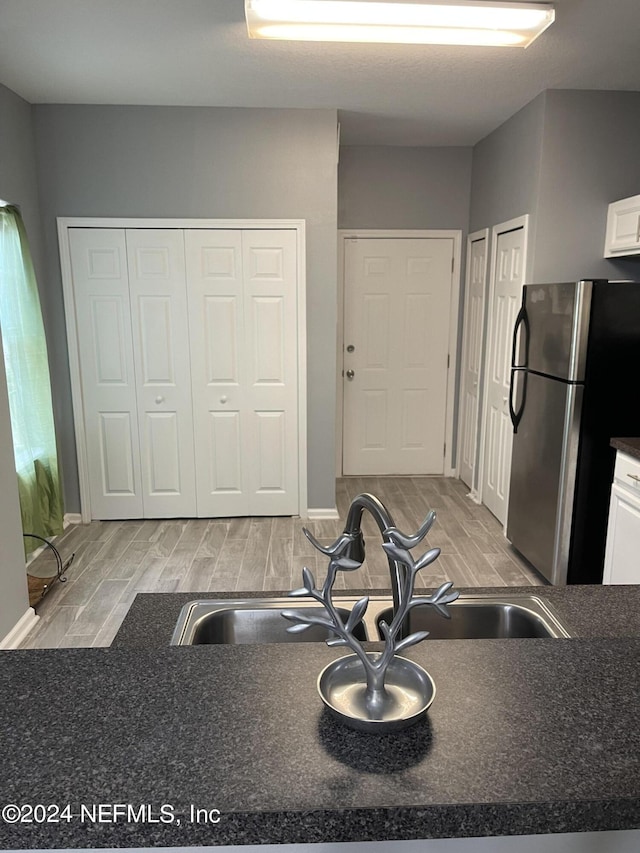 kitchen with white cabinetry, sink, and stainless steel refrigerator