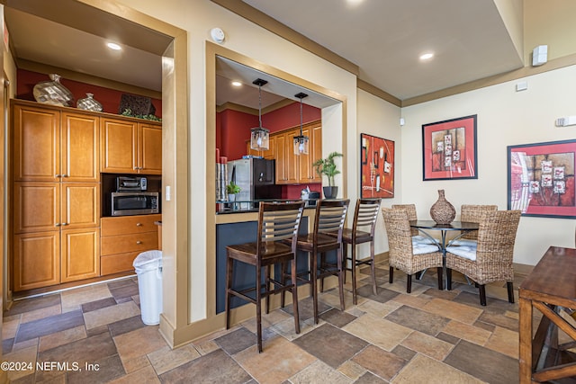 kitchen with appliances with stainless steel finishes, brown cabinetry, stone tile flooring, and baseboards