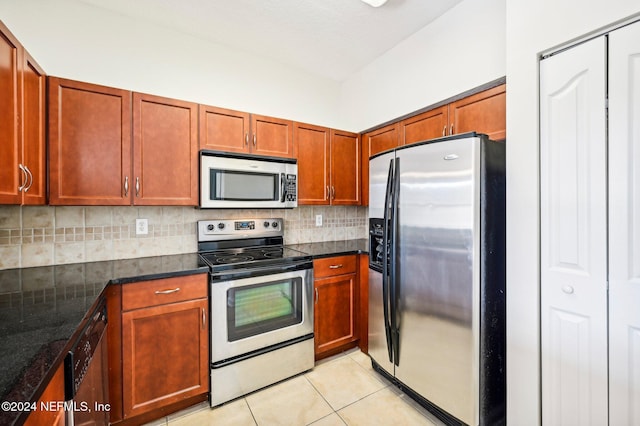 kitchen with light tile patterned flooring, stainless steel appliances, decorative backsplash, brown cabinetry, and dark stone countertops