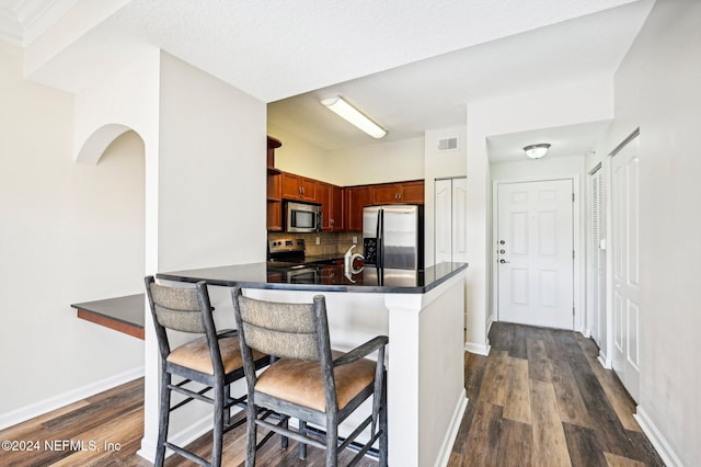 kitchen with tasteful backsplash, dark countertops, visible vents, appliances with stainless steel finishes, and a kitchen bar