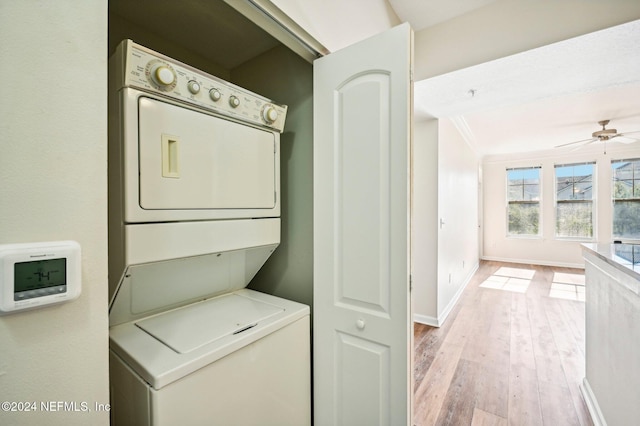 clothes washing area featuring laundry area, a ceiling fan, baseboards, light wood finished floors, and stacked washer and clothes dryer