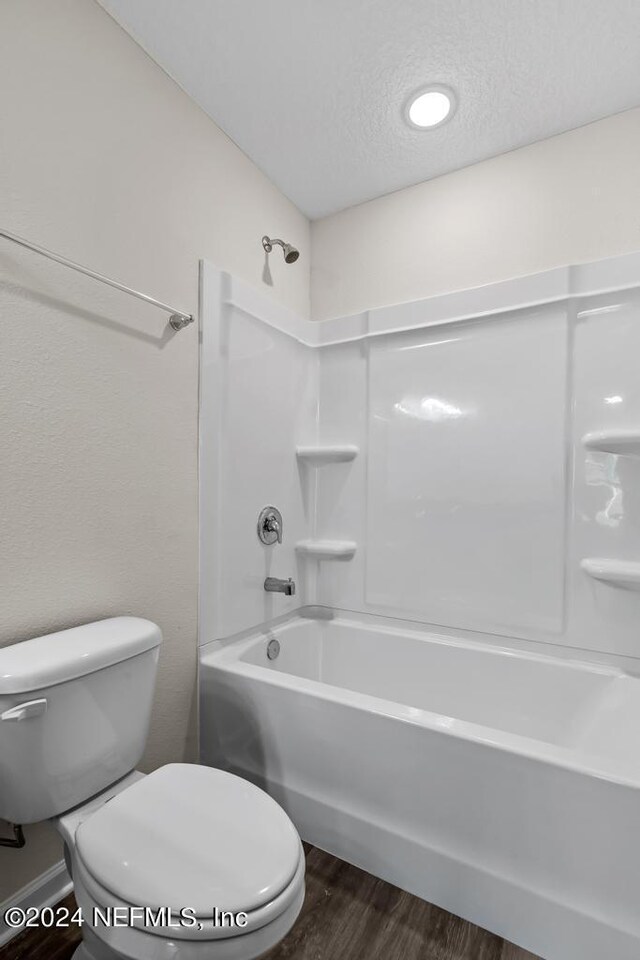 bathroom with wood-type flooring, a textured ceiling, toilet, and tub / shower combination