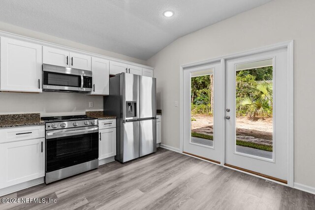 kitchen with dark stone counters, light hardwood / wood-style flooring, stainless steel appliances, white cabinets, and lofted ceiling