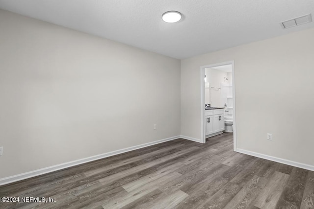 unfurnished bedroom featuring baseboards, visible vents, connected bathroom, dark wood-style floors, and a textured ceiling