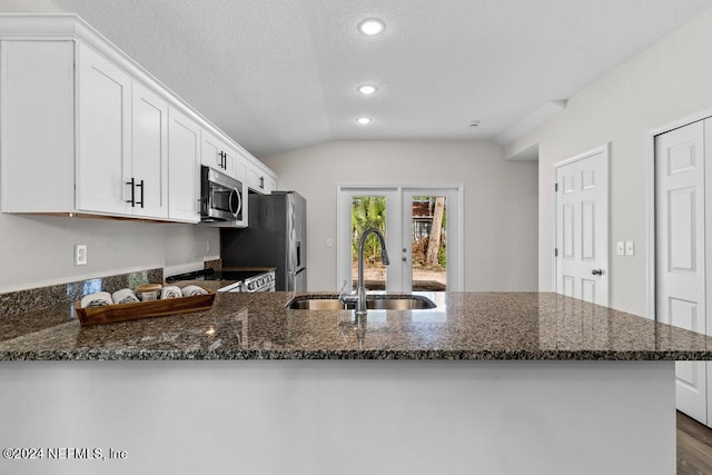 kitchen with stainless steel appliances, a peninsula, a sink, white cabinets, and dark stone counters