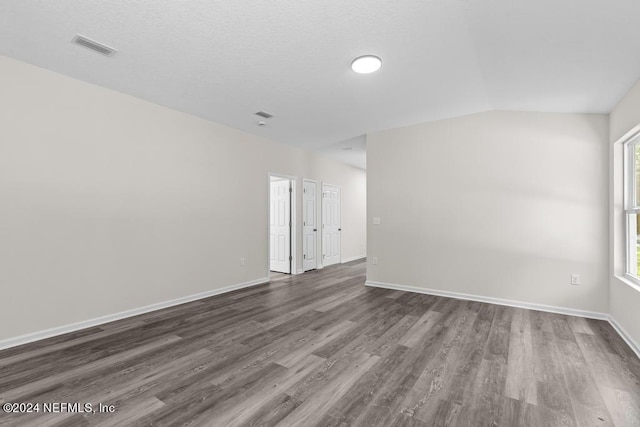 empty room with lofted ceiling, dark wood-type flooring, visible vents, and baseboards