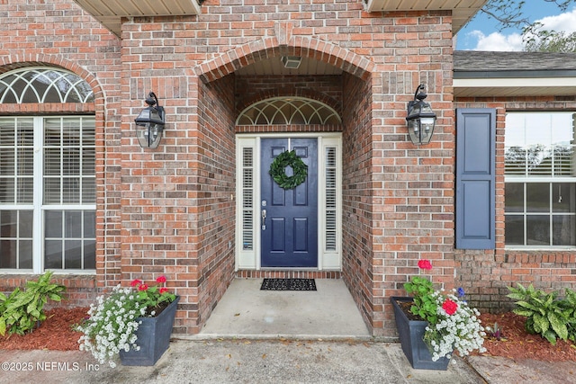 view of exterior entry featuring roof with shingles and brick siding