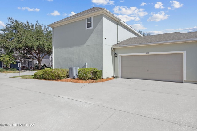 view of side of property with central air condition unit, stucco siding, driveway, and a garage