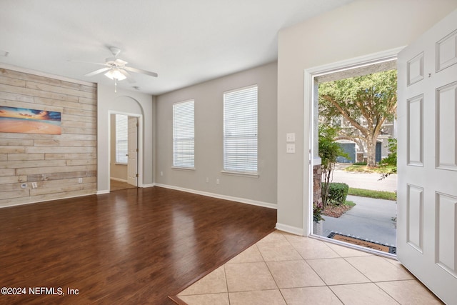 entrance foyer with an accent wall, baseboards, wood walls, light tile patterned floors, and a ceiling fan