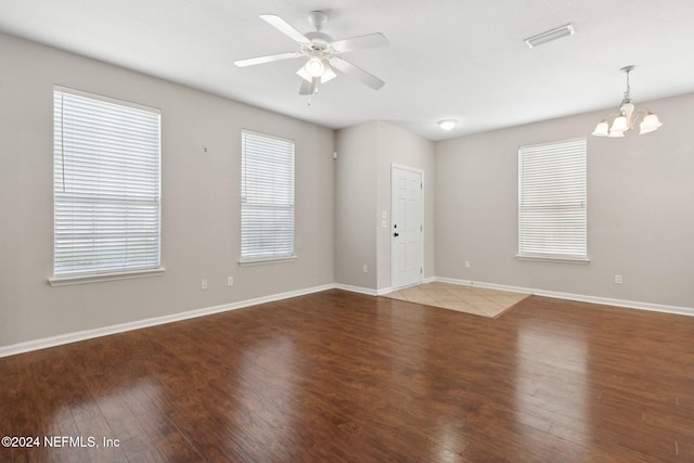 spare room with ceiling fan with notable chandelier, plenty of natural light, wood finished floors, and baseboards