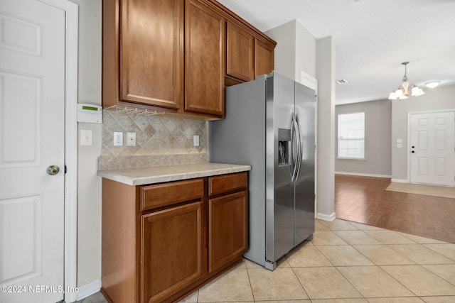 kitchen featuring brown cabinets, stainless steel fridge, an inviting chandelier, light tile patterned flooring, and light countertops