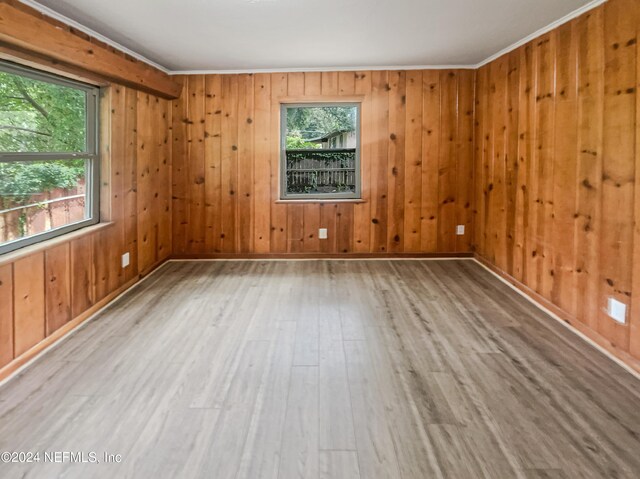 spare room with light wood-type flooring, wood walls, and ornamental molding