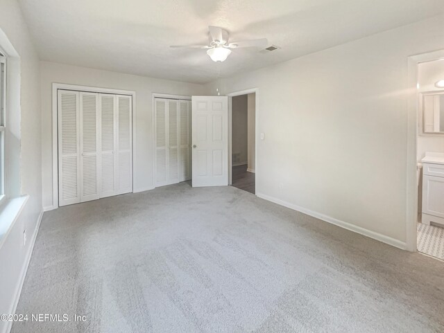 unfurnished bedroom featuring light colored carpet, connected bathroom, two closets, and ceiling fan