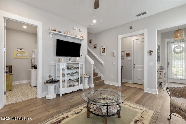 living room with hardwood / wood-style flooring, ceiling fan, and a textured ceiling