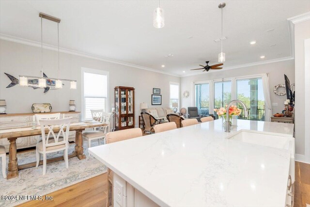 kitchen with sink, crown molding, decorative light fixtures, an island with sink, and light hardwood / wood-style floors