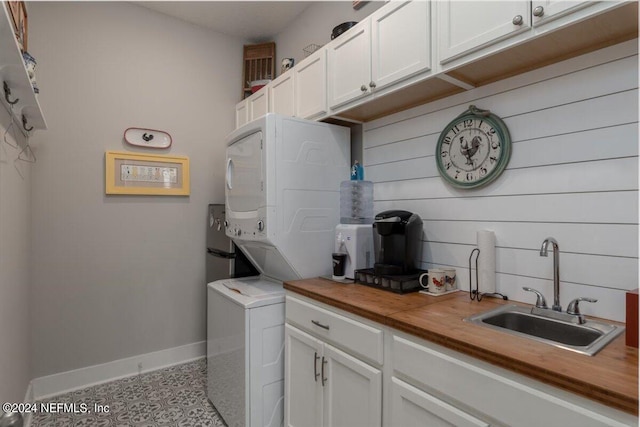 laundry room with cabinets, stacked washer / drying machine, sink, and wood walls