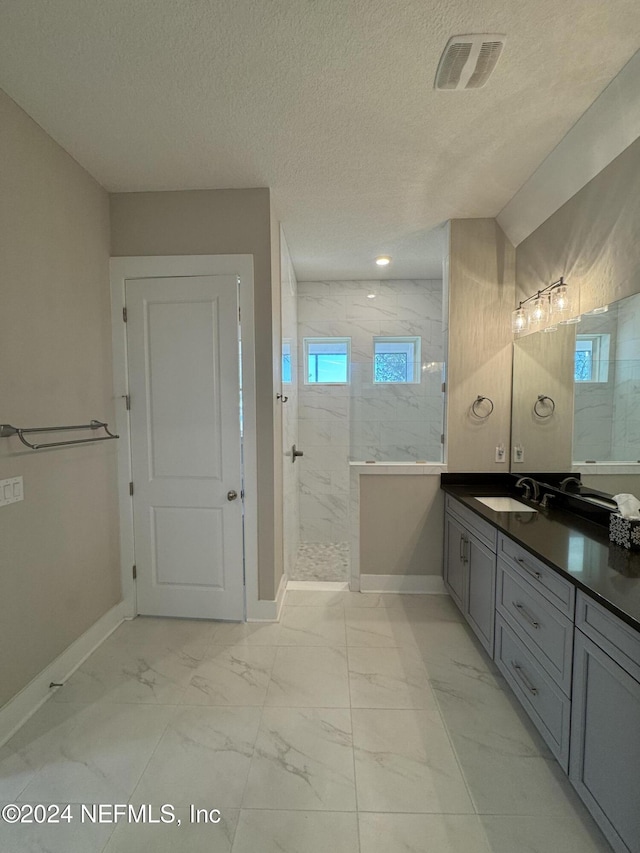 bathroom with vanity, a tile shower, and a textured ceiling