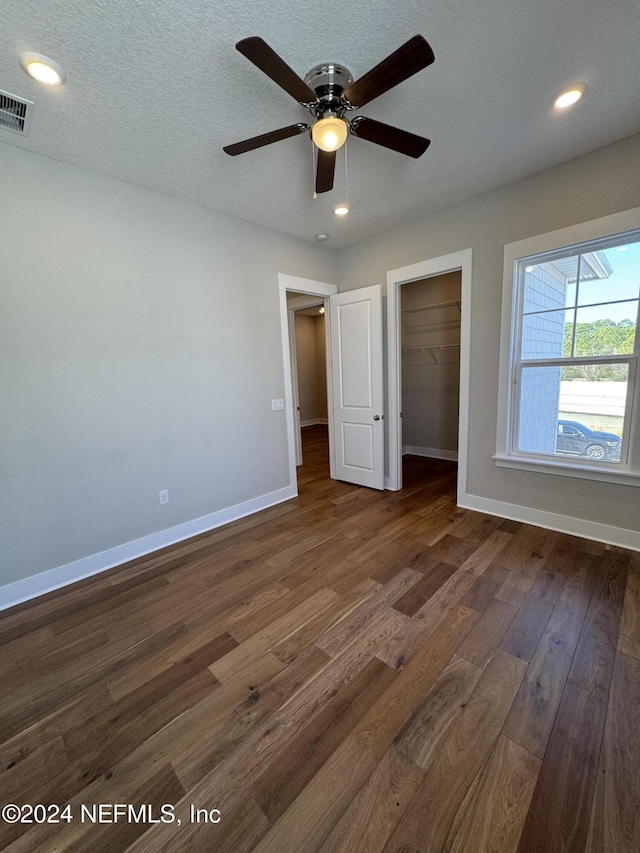 unfurnished bedroom with dark hardwood / wood-style flooring, a spacious closet, ceiling fan, a textured ceiling, and a closet