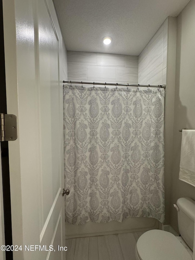 bathroom with shower / tub combo, a textured ceiling, and toilet