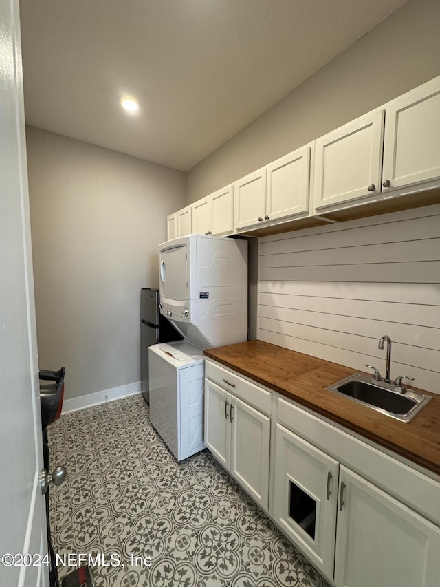 kitchen with white cabinetry, stacked washer / drying machine, sink, and wood counters