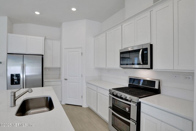 kitchen featuring appliances with stainless steel finishes, sink, light hardwood / wood-style flooring, and white cabinets