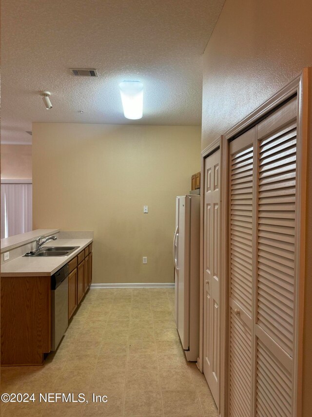 kitchen with dishwasher, sink, white fridge, and a textured ceiling