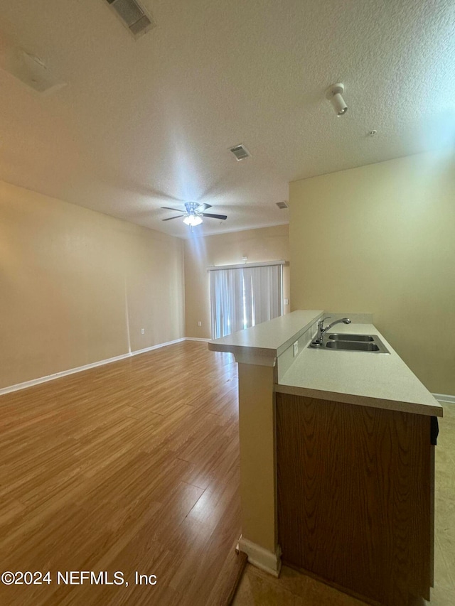 kitchen with ceiling fan, sink, a textured ceiling, and light wood-type flooring