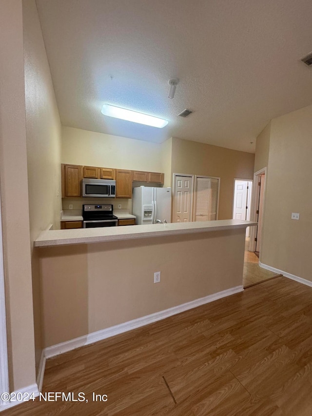 kitchen featuring hardwood / wood-style flooring, stainless steel appliances, kitchen peninsula, and a textured ceiling