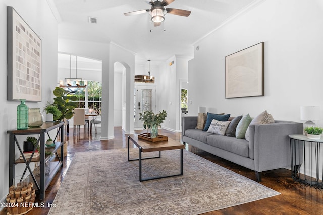 living room with dark wood-type flooring, ceiling fan with notable chandelier, and ornamental molding