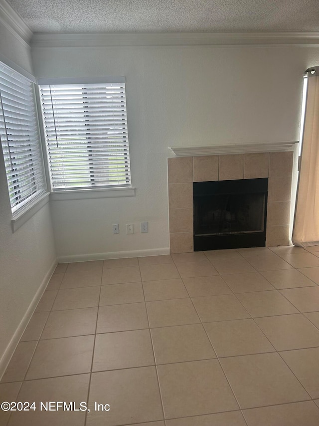 unfurnished living room featuring a textured ceiling, crown molding, a tiled fireplace, and light tile patterned floors