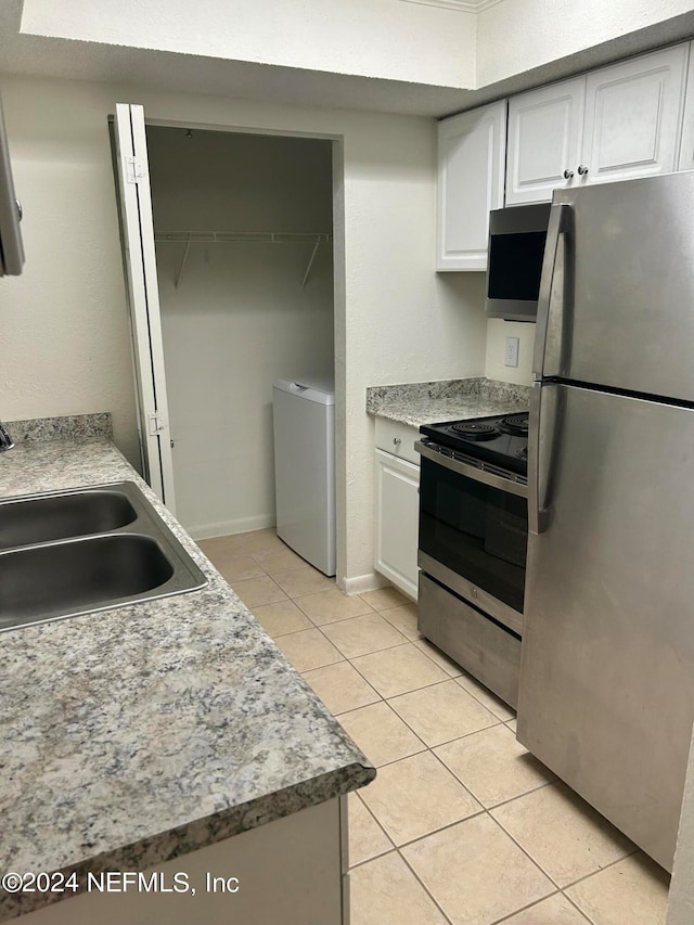 kitchen with light tile patterned floors, white cabinetry, washer / dryer, and stainless steel appliances