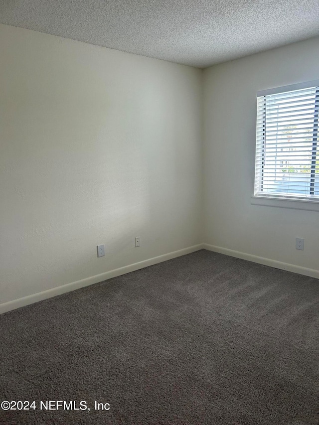 spare room with dark carpet and a textured ceiling