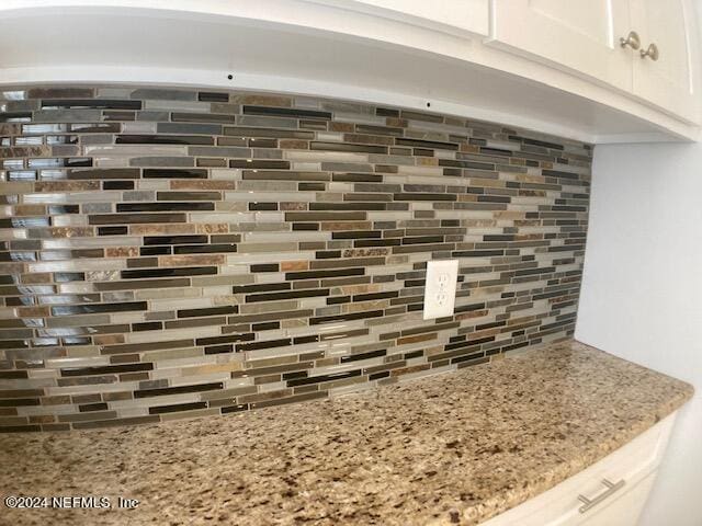 details featuring tasteful backsplash, white cabinetry, and light stone counters