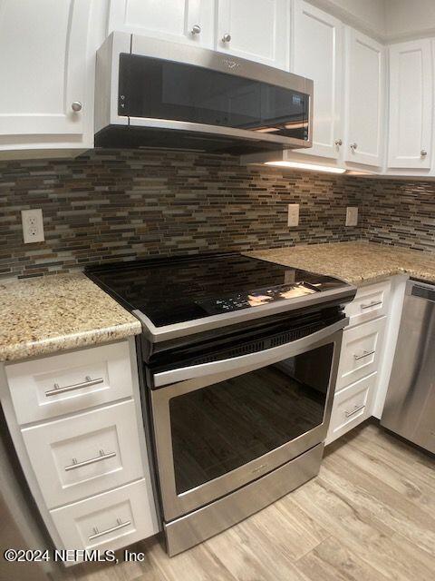 kitchen featuring white cabinetry, light stone counters, light hardwood / wood-style flooring, and stainless steel appliances